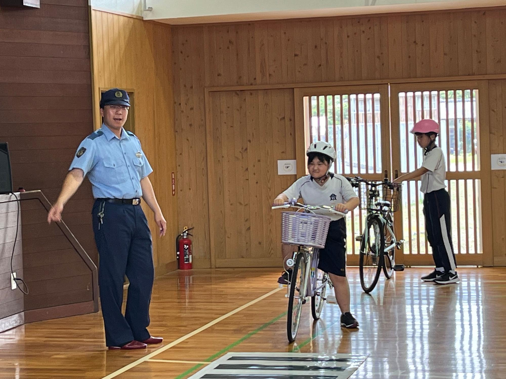 体育館で児童たちが警察官の指導で自転車交通安全教室に参加している写真