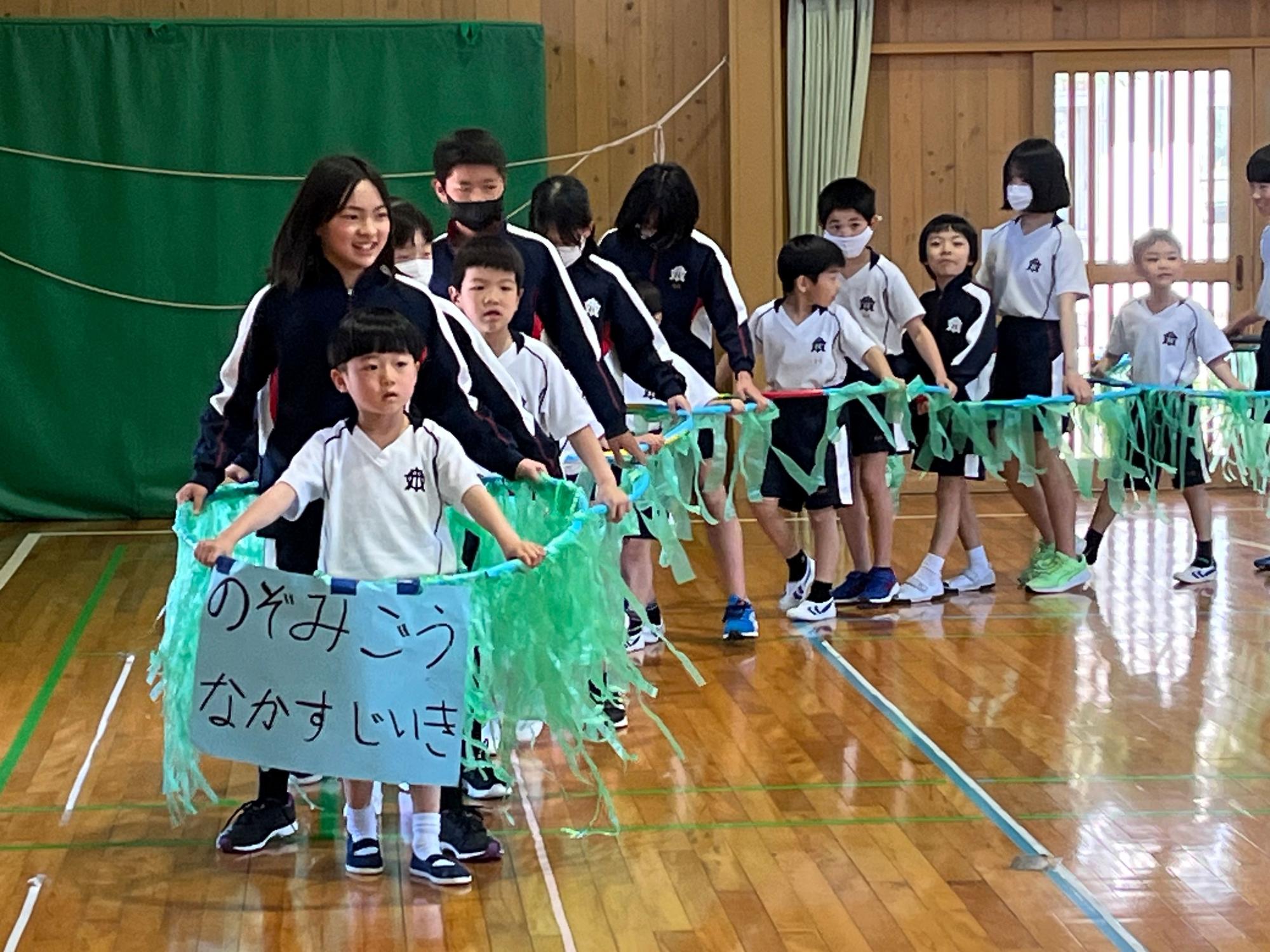 体育館で児童たちが列になってパフォーマンスをしている写真