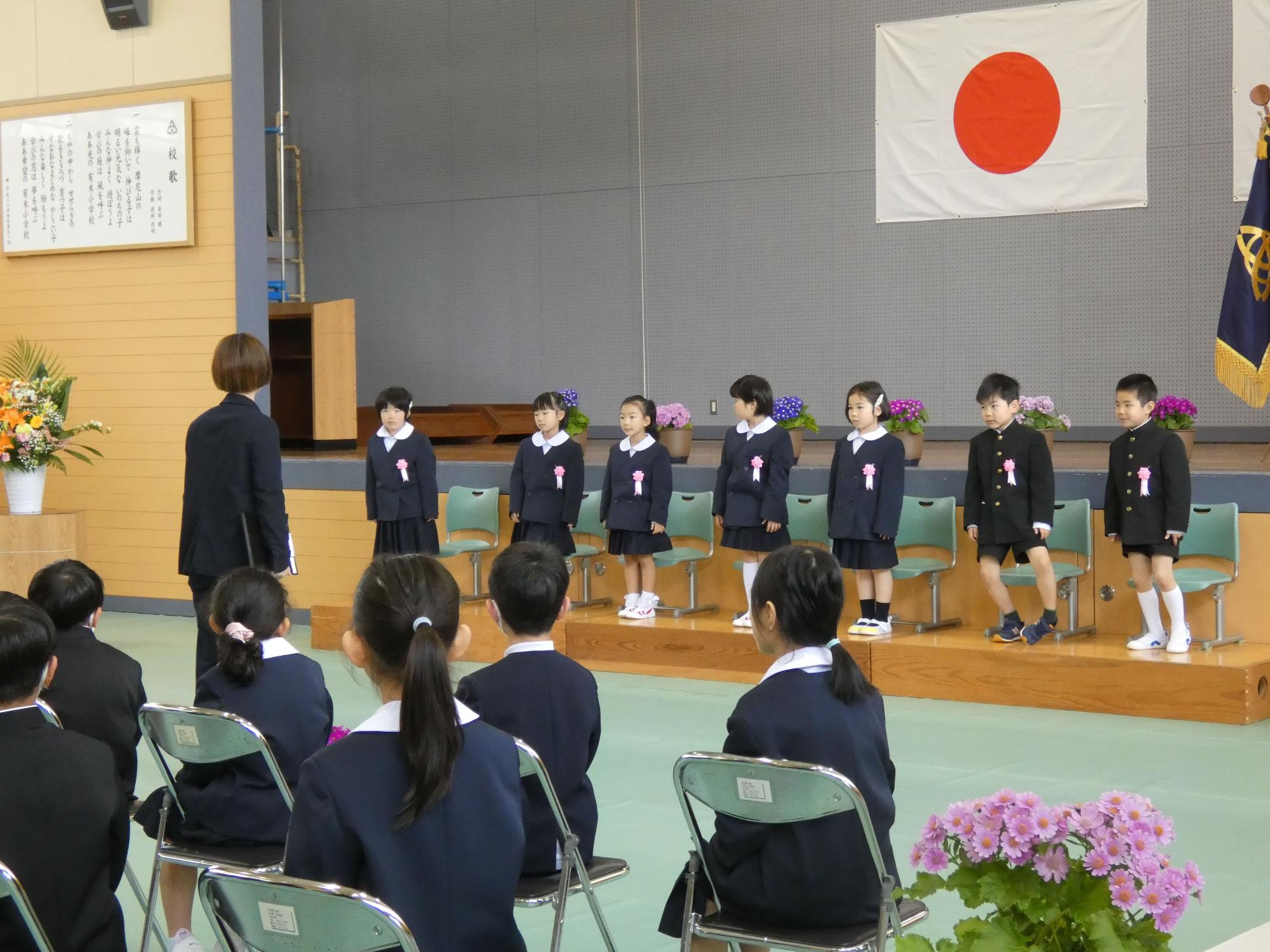 体育館の舞台で新入生が担任の先生の前に並んでいる写真