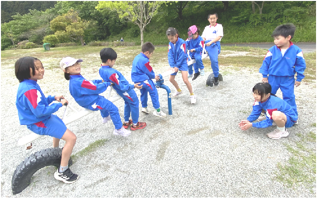 公園で青い体操服を着た児童たちがシーソーで遊んでいる写真