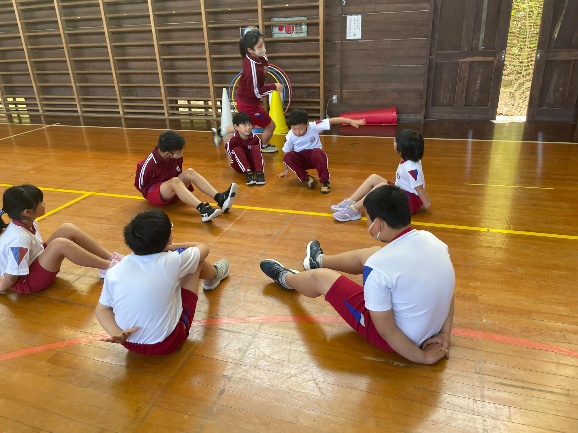 体育館で児童たちが円になって体育座りをして話し合っている写真