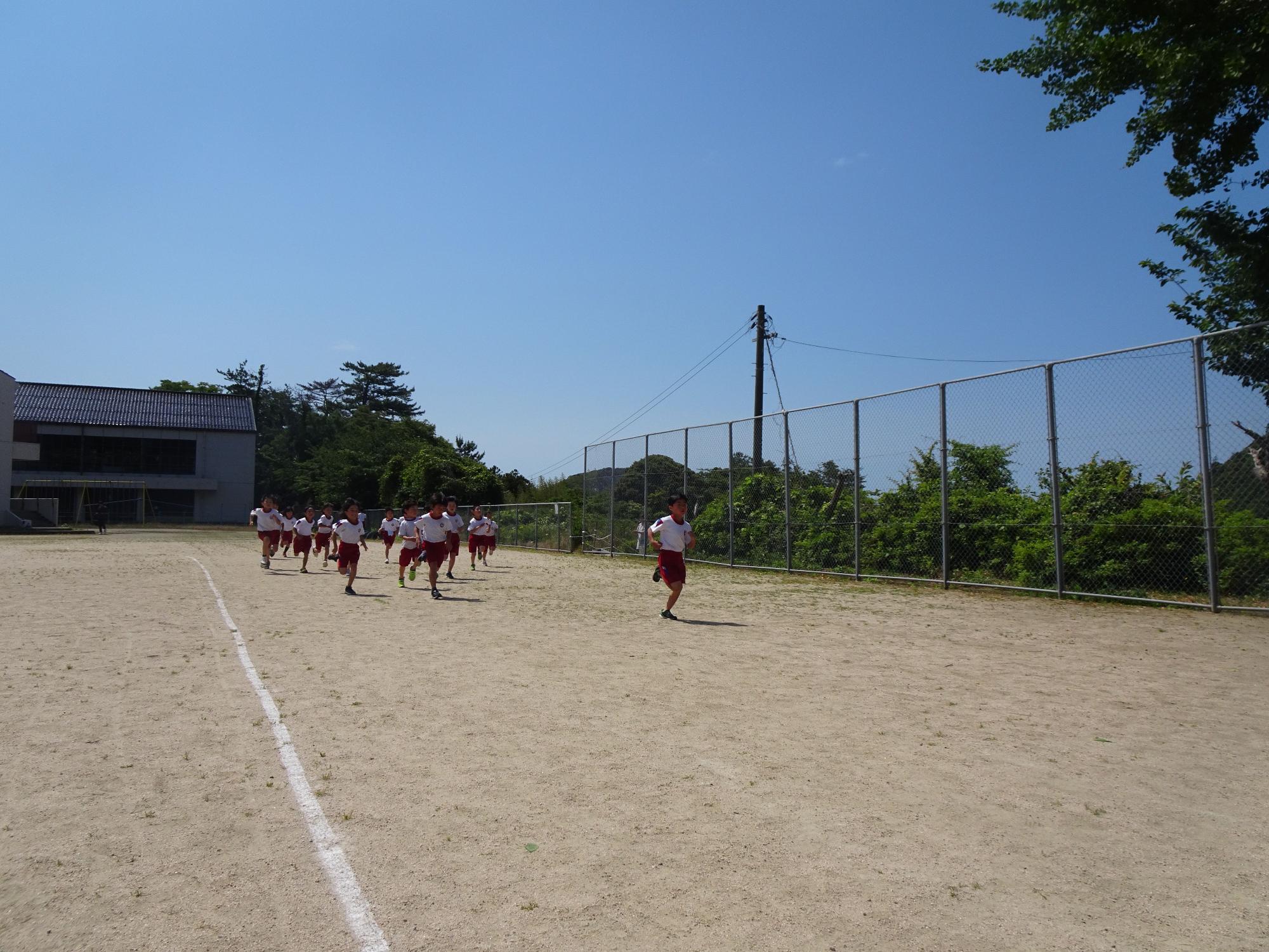 青空の下校庭で体育着姿の児童たちが一斉に走っている写真