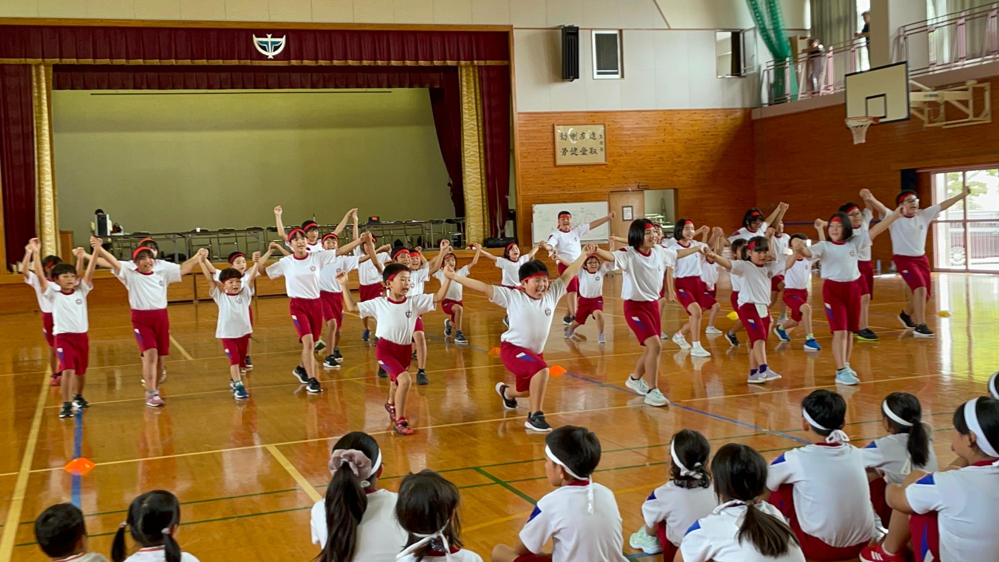 体育館で体育着を着た大勢の児童たちが元気にダンスをしている写真