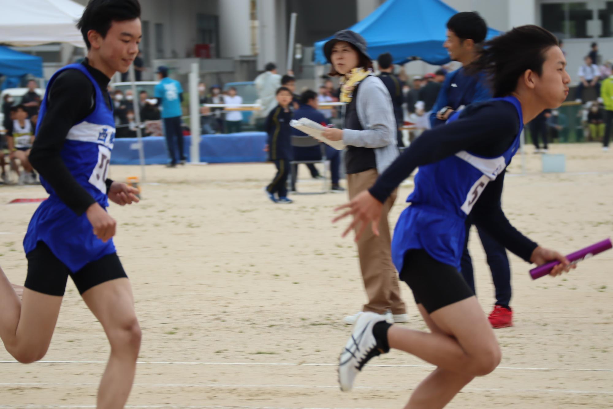 陸上競技場で生徒たちがリレーのバトンをつないで走っている写真