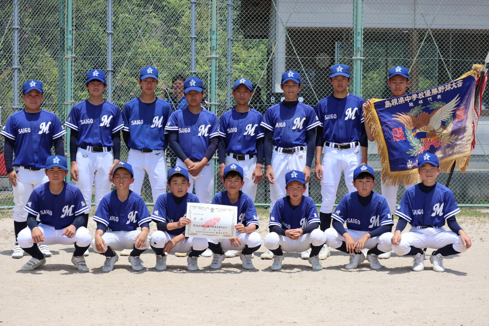 野球場で野球部の生徒たちが優勝旗と賞状を持って記念撮影をしている写真