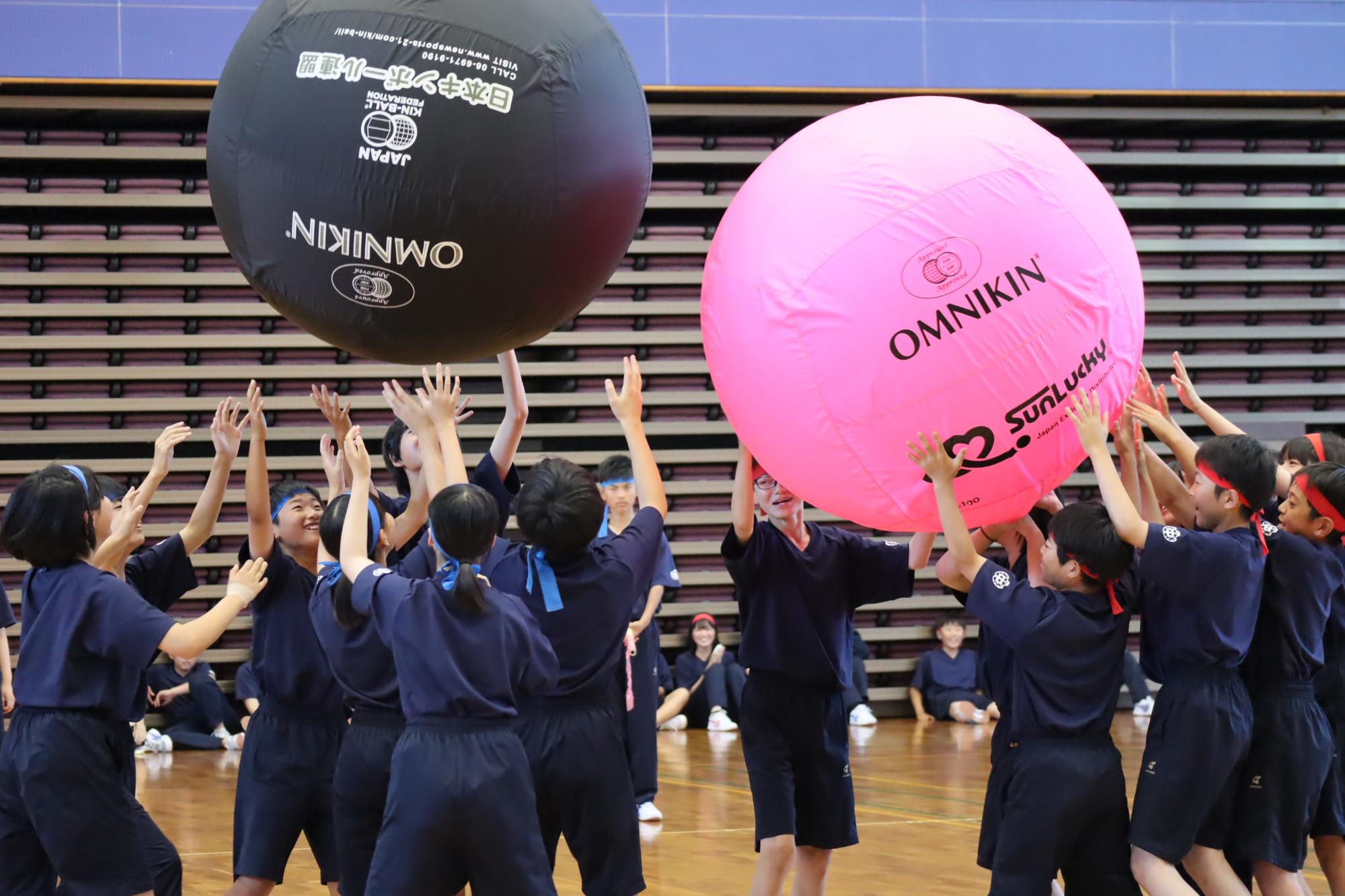 体育館で生徒たちが大玉を使って競技をしている写真