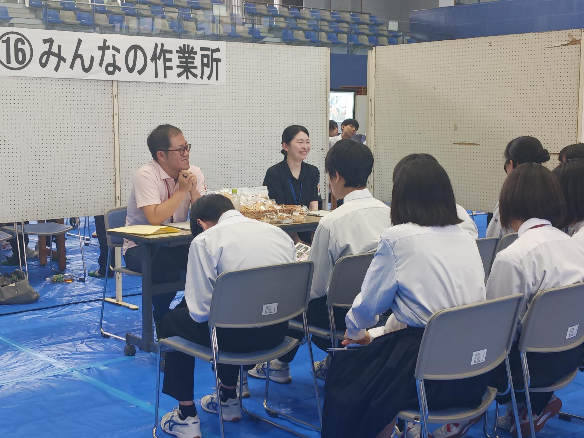体育館で生徒たちが企業や施設の説明を聞いている写真