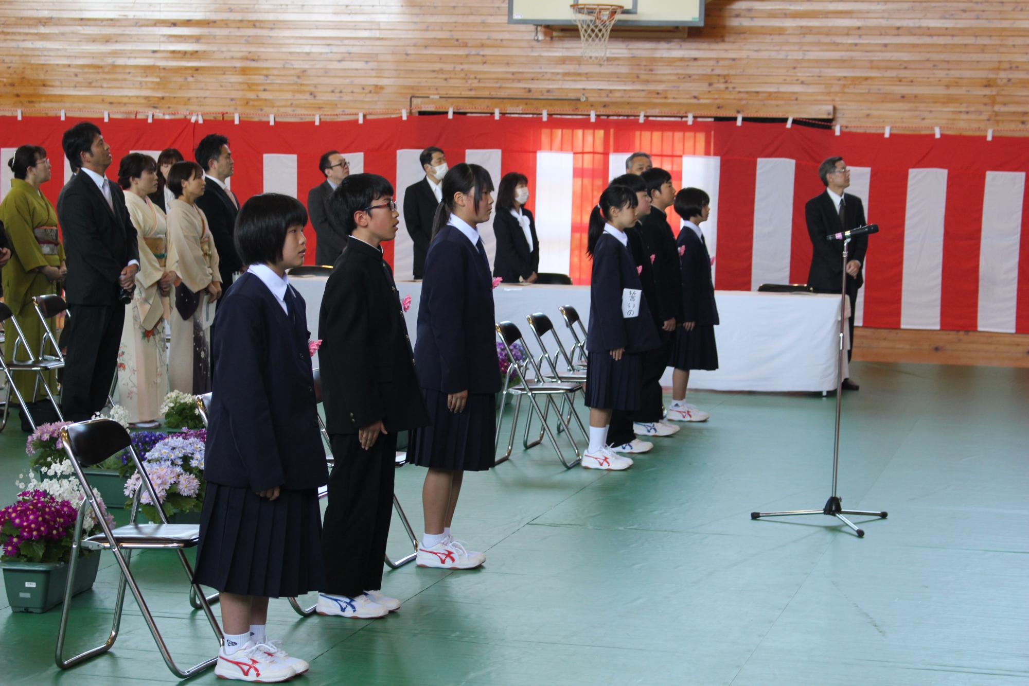 体育館で保護者と教職員が見守る中、入学式に臨む新入生の写真