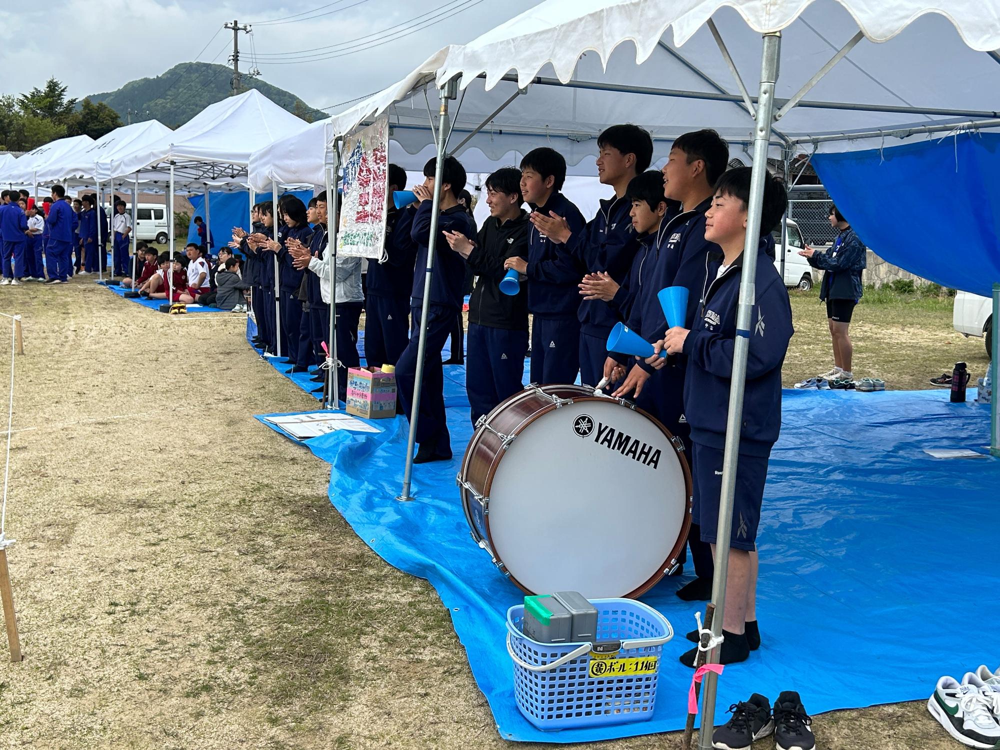 校庭に設置されたテントの下から太鼓と拍手で応援する生徒たちの写真