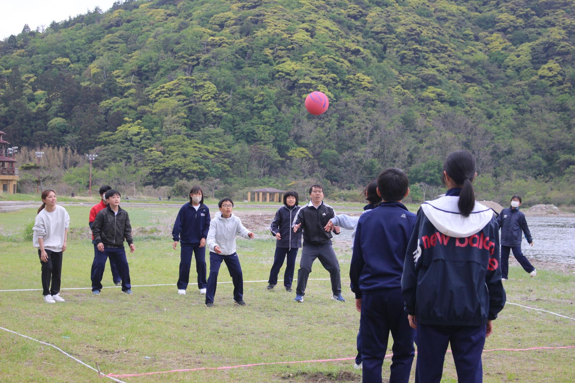 河原の広場で生徒たちがボールを使ってレクリエーションを楽しんでいる写真