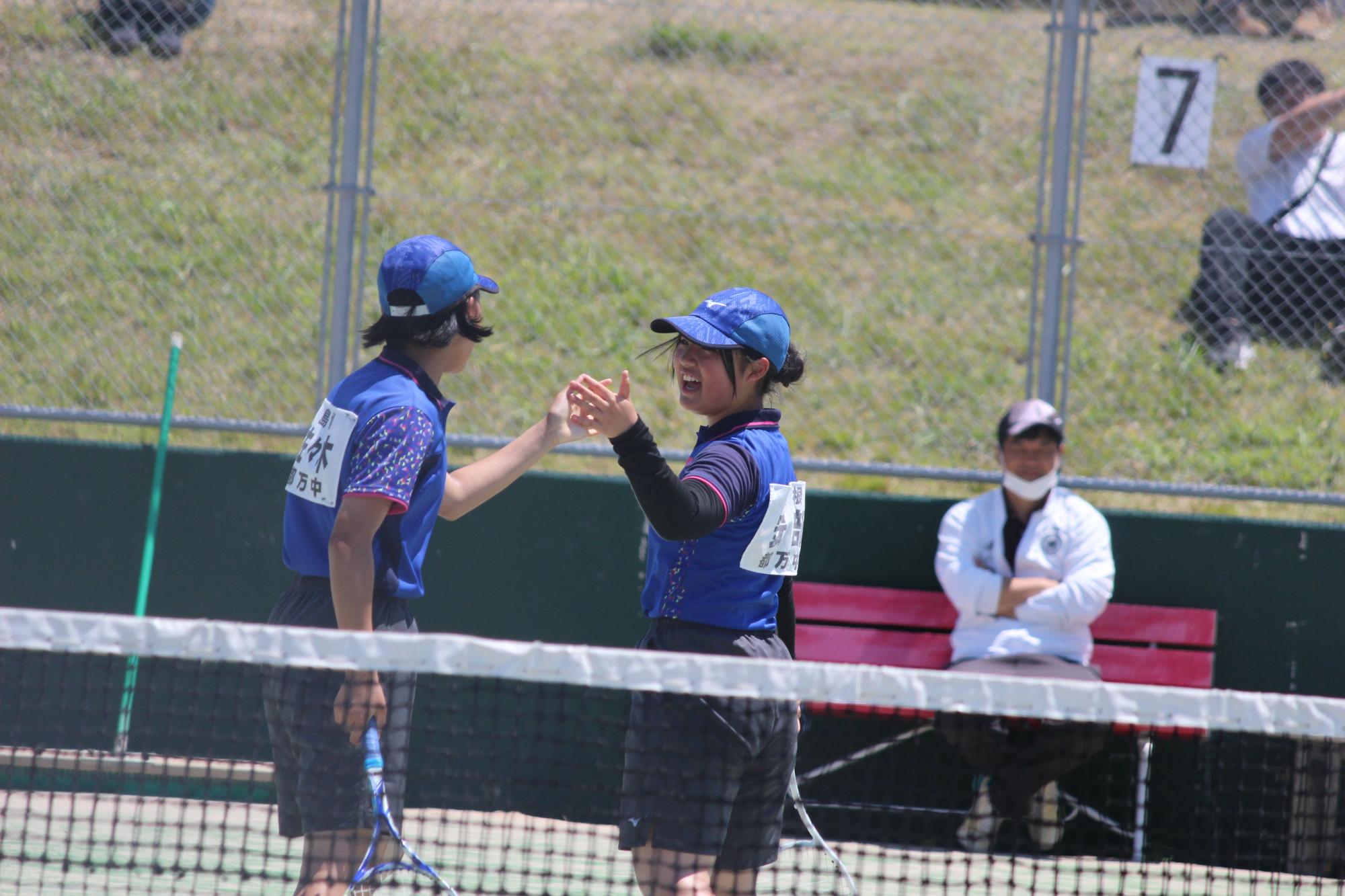 テニスコートでハイタッチを交わす生徒たちの写真