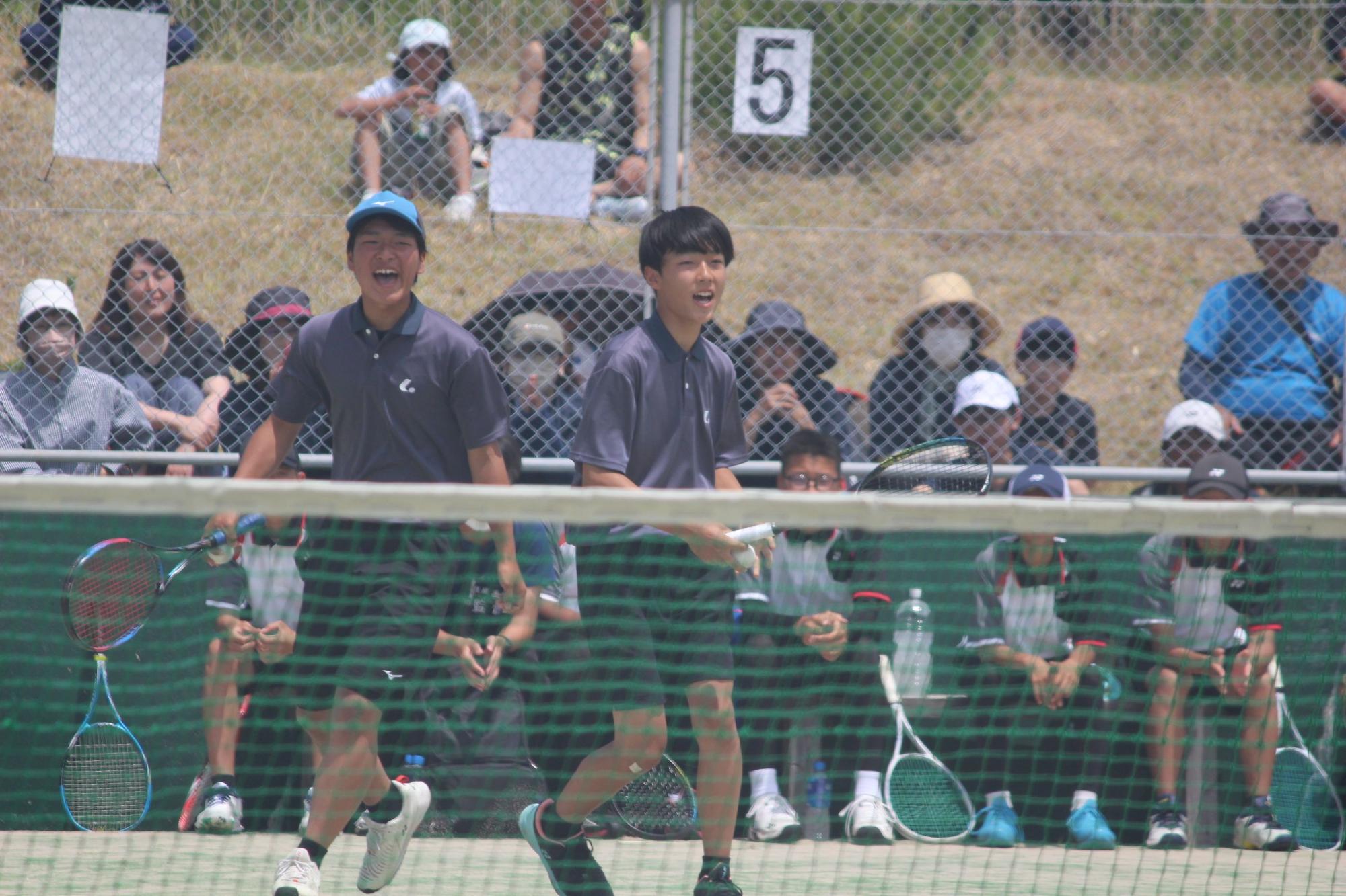 テニスコートで笑顔でプレーする男子生徒ペアの写真