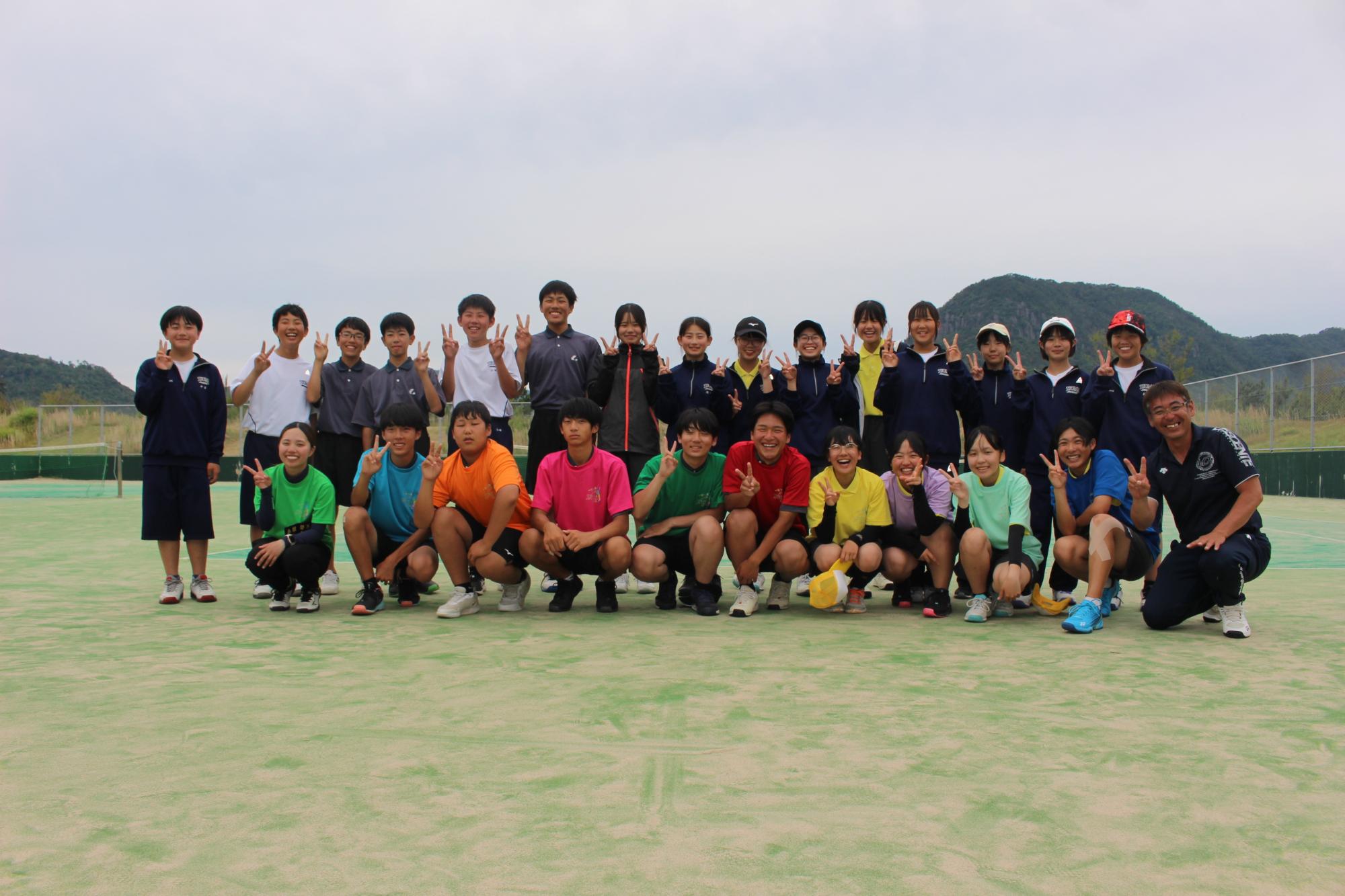 テニスコートで色とりどりのシャツを着た生徒たちが集合して記念撮影をしている写真
