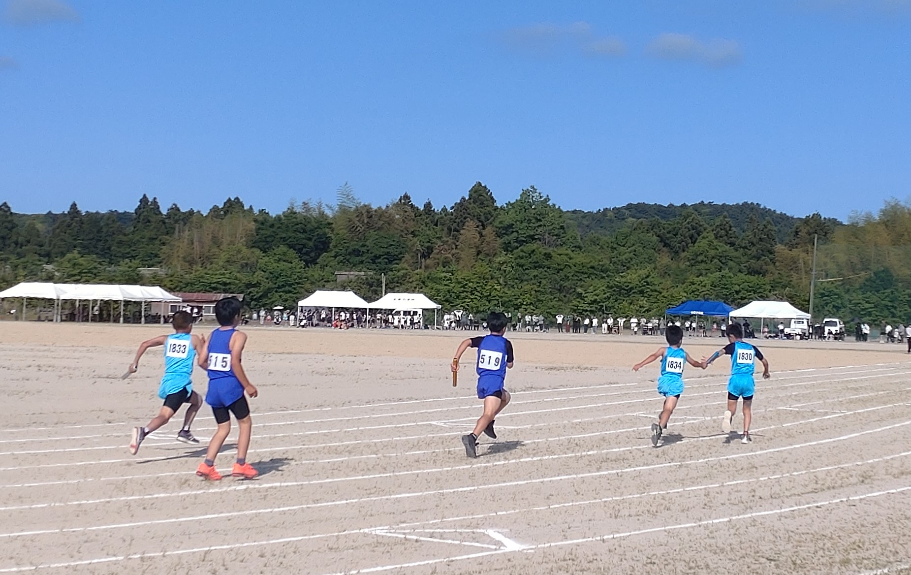 グラウンドのトラックで児童たちがバトンをつないで走っている写真