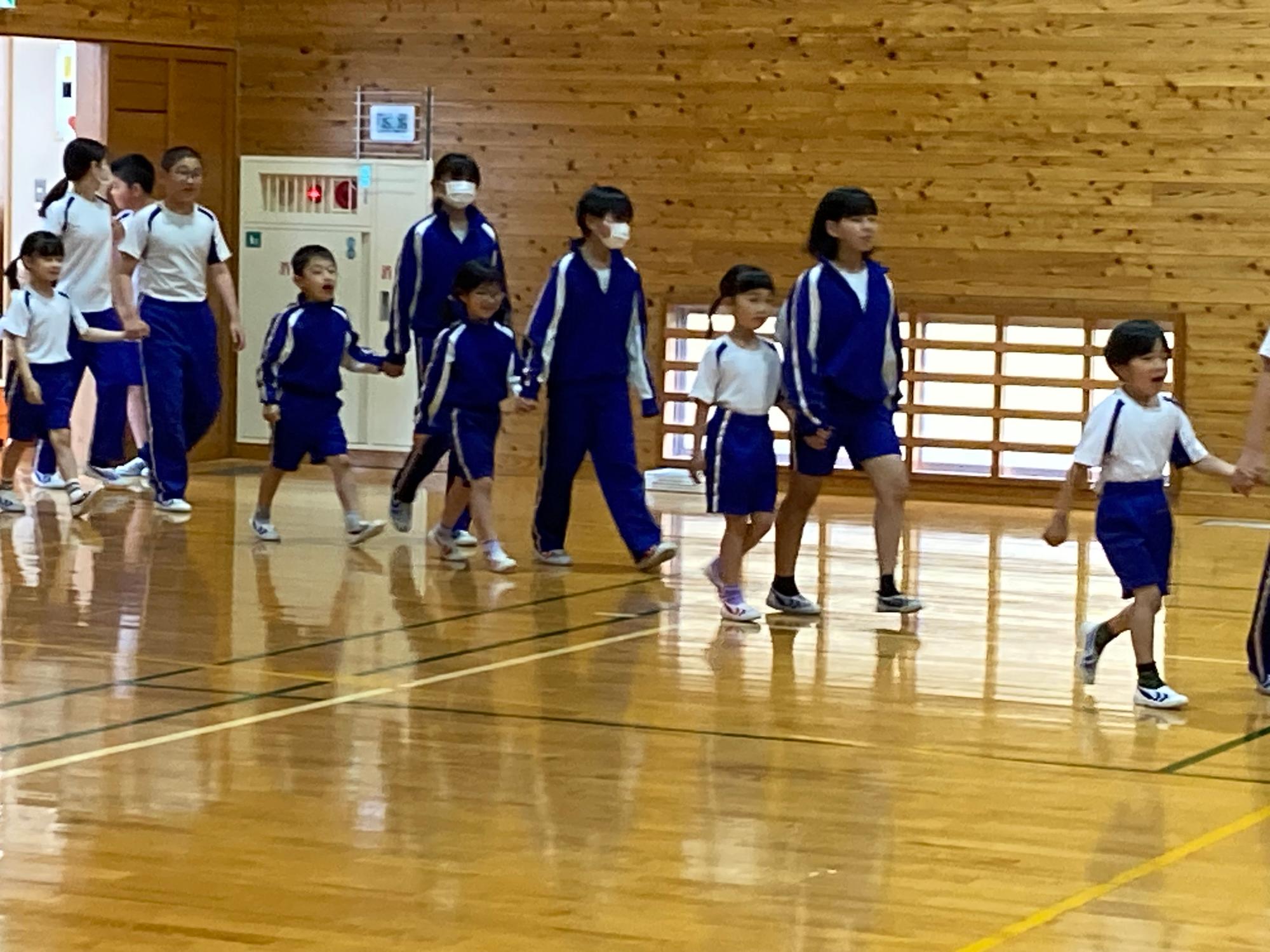 体育館で上級生が新入生の手を引いて入場している写真