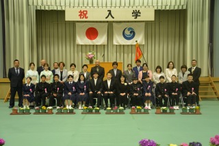 体育館で新入生と保護者、教職員が並んで記念撮影をしている写真