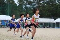 グラウンドでユニフォームを着た女子選手たちがリレーのバトンを持って走っている写真