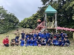 公園の遊具前で子どもたちと指導者が集合写真を撮っている写真