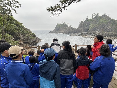遊具のある公園で青い体操服を着た児童たちが集合して記念撮影をしている写真