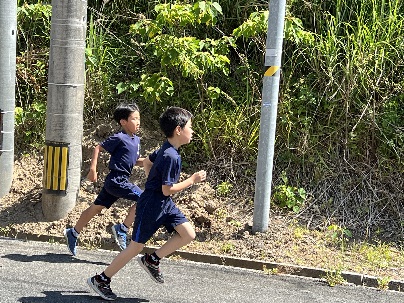 道沿いの日向を体操服を着た男子児童が並んで競走している写真