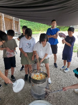 キャンプ場で子どもたちが鍋でカレーを調理している写真