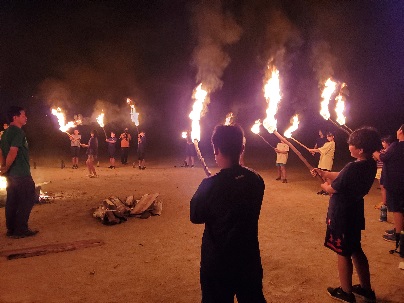 夜のキャンプ場で子どもたちが松明を持って円になっている写真