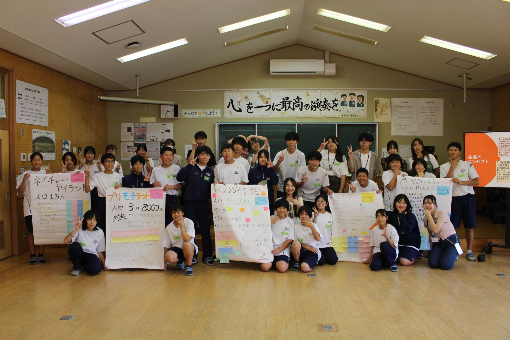 教室で班ごとに作成したポスターを持ち、全員で集合写真を撮っている写真