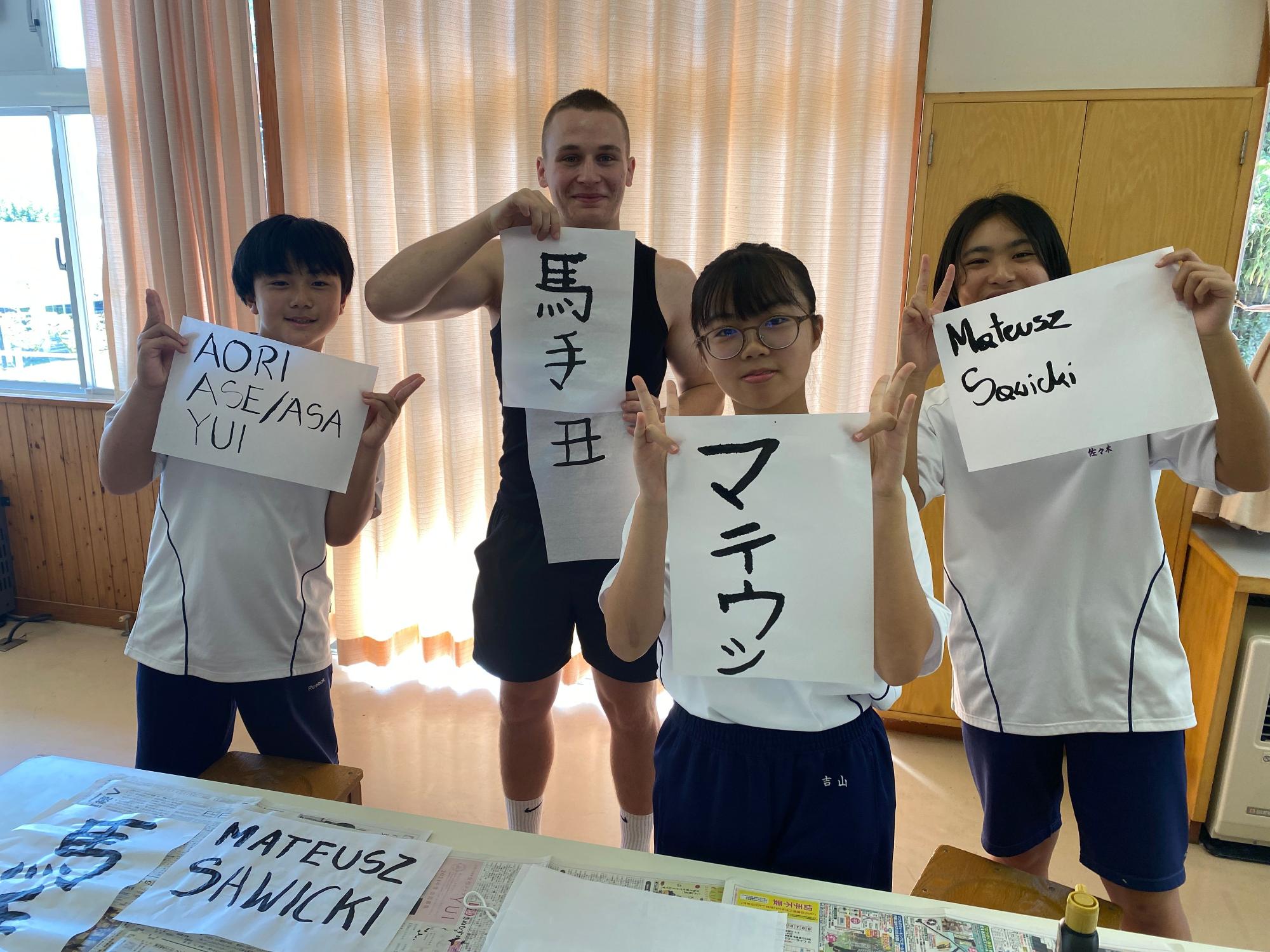 書道作品を手に日本の生徒たちと外国の生徒たちが並んでいる写真