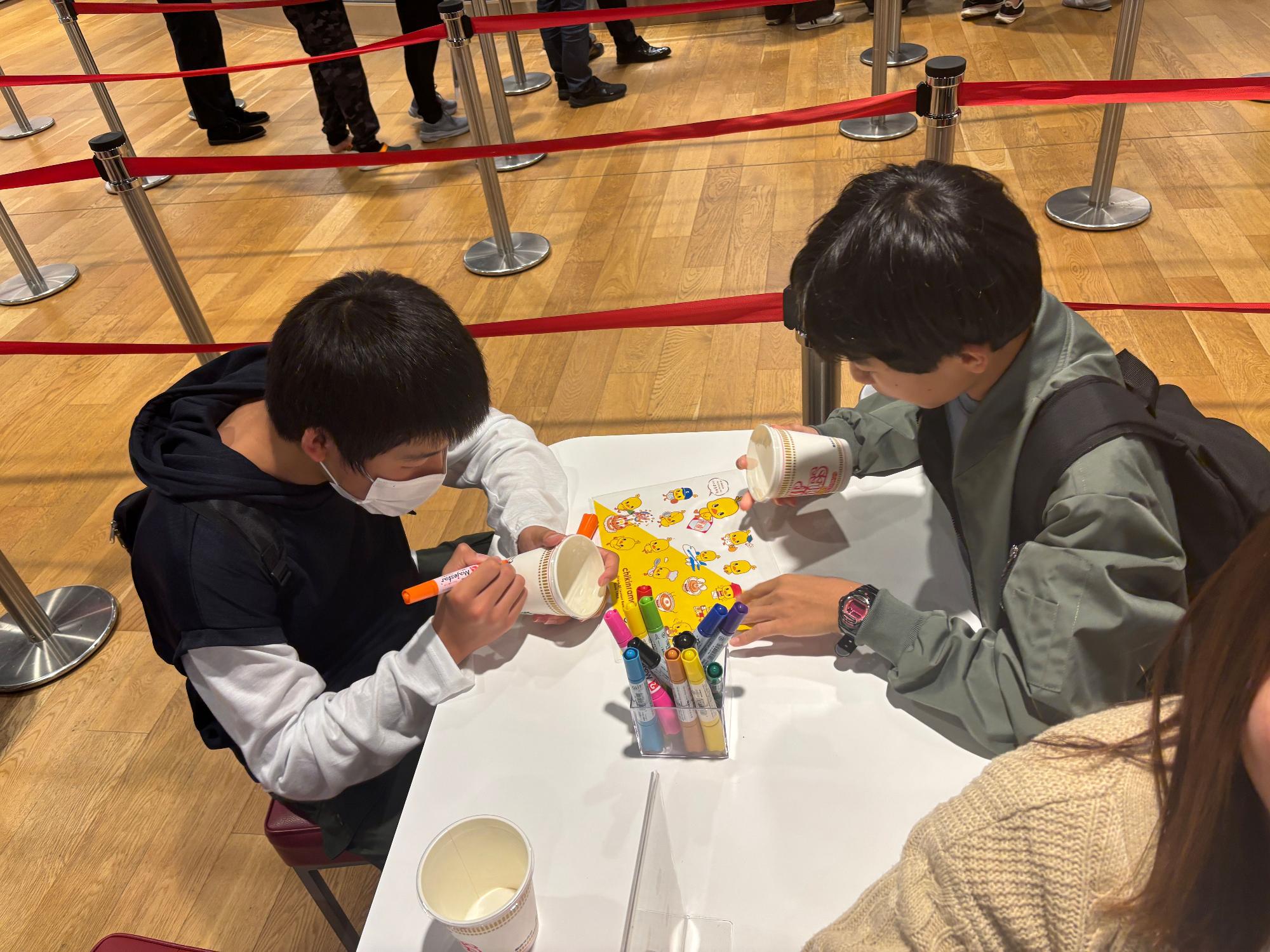 カップにイラストを描いている生徒たちの写真