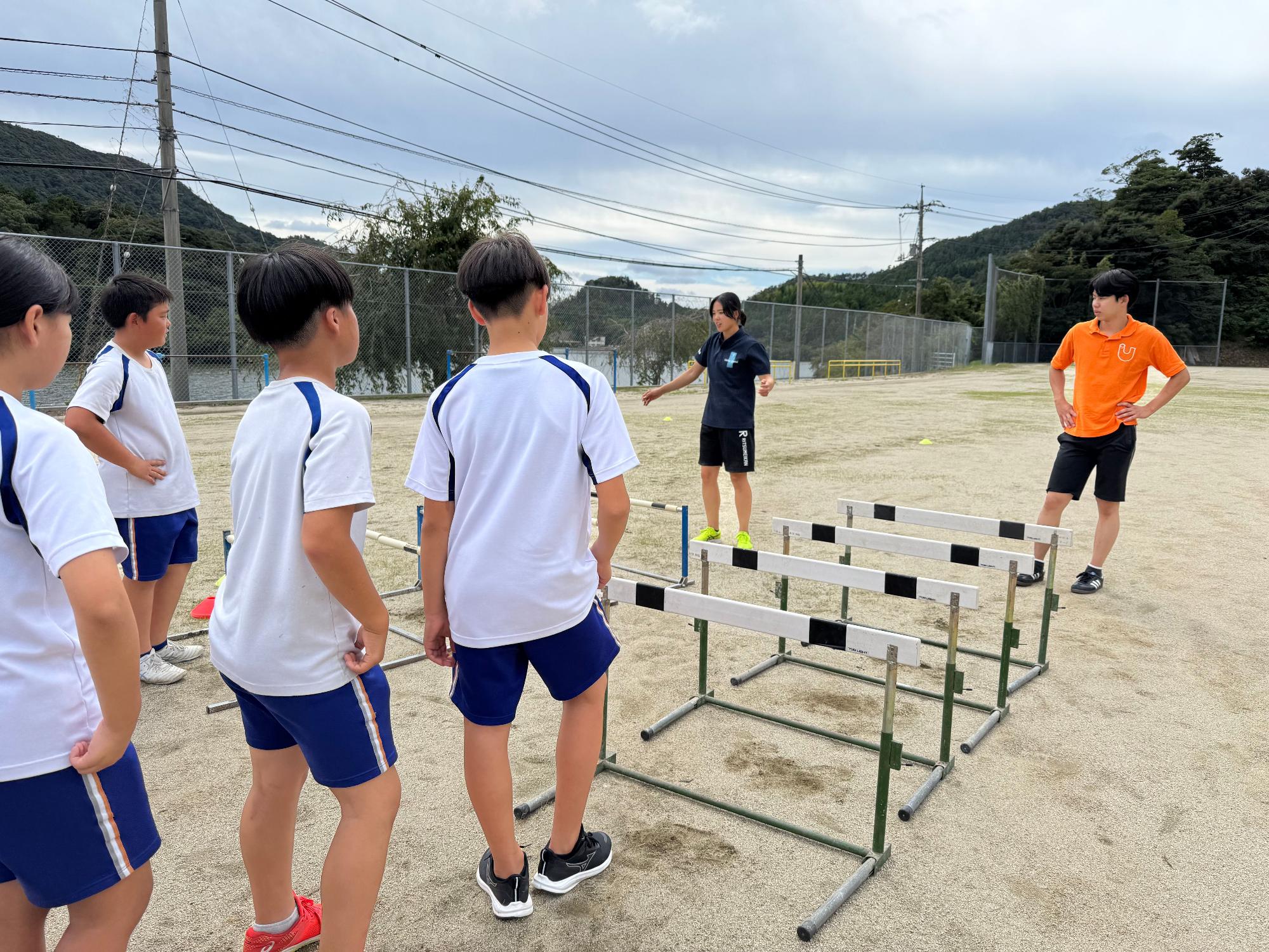 校庭で先生と児童がハードル走の練習をしている写真
