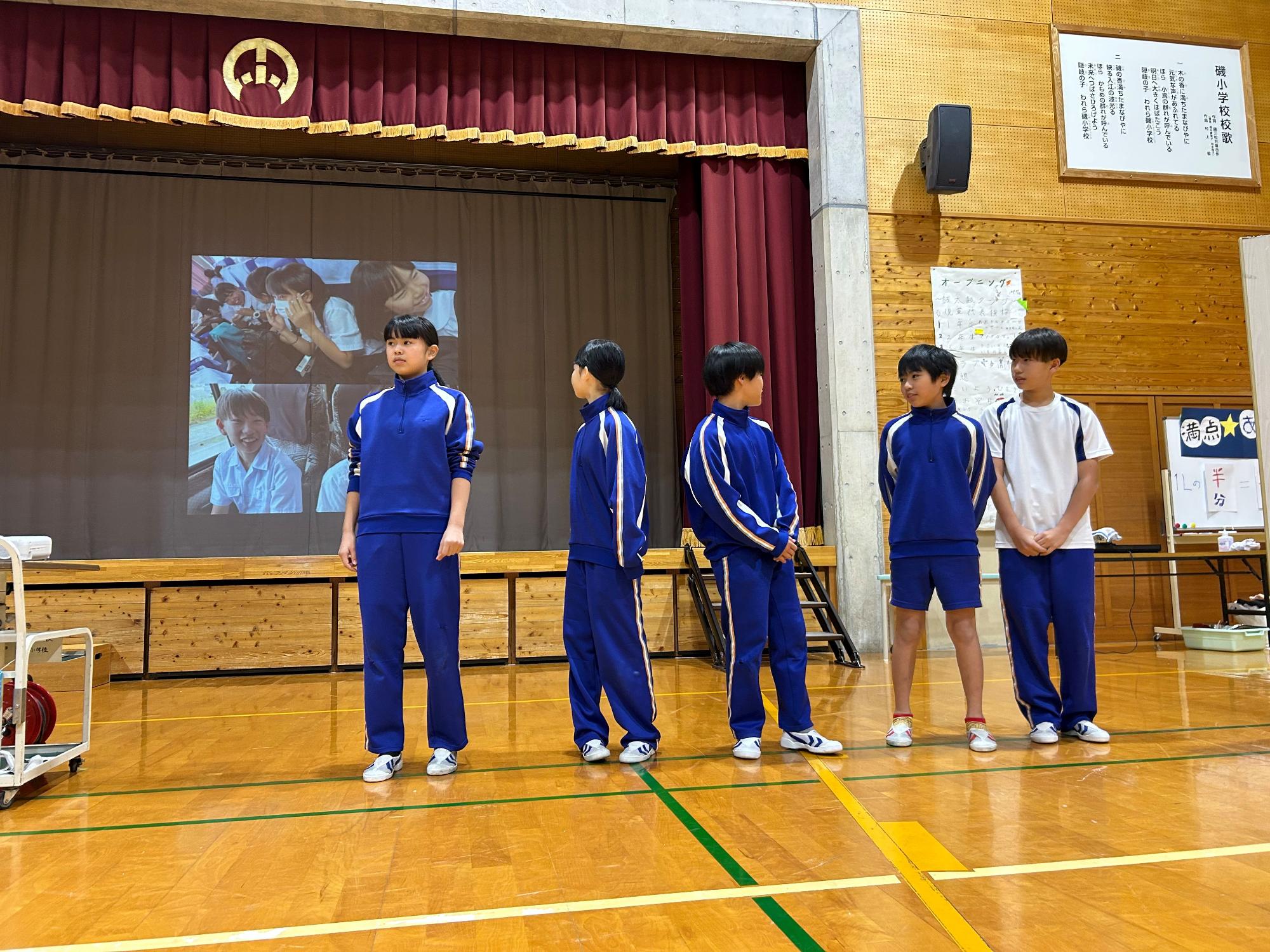 体育館の舞台前で児童が発表している写真