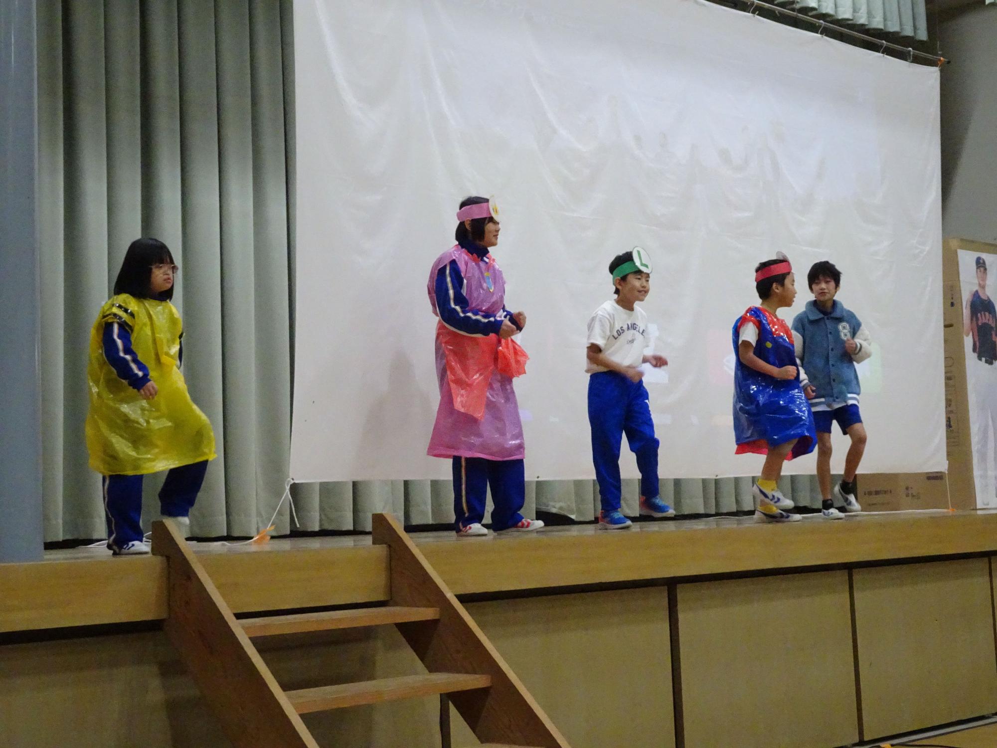 体育館の舞台で子どもたちがカラフルな衣装を着て劇をしている写真