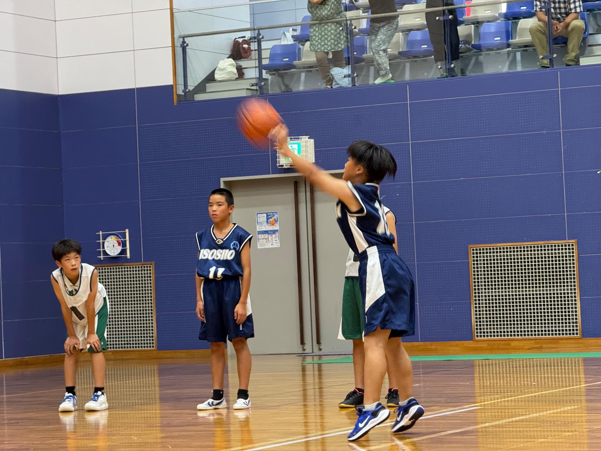 体育館で児童がバスケットボールの試合をしている写真