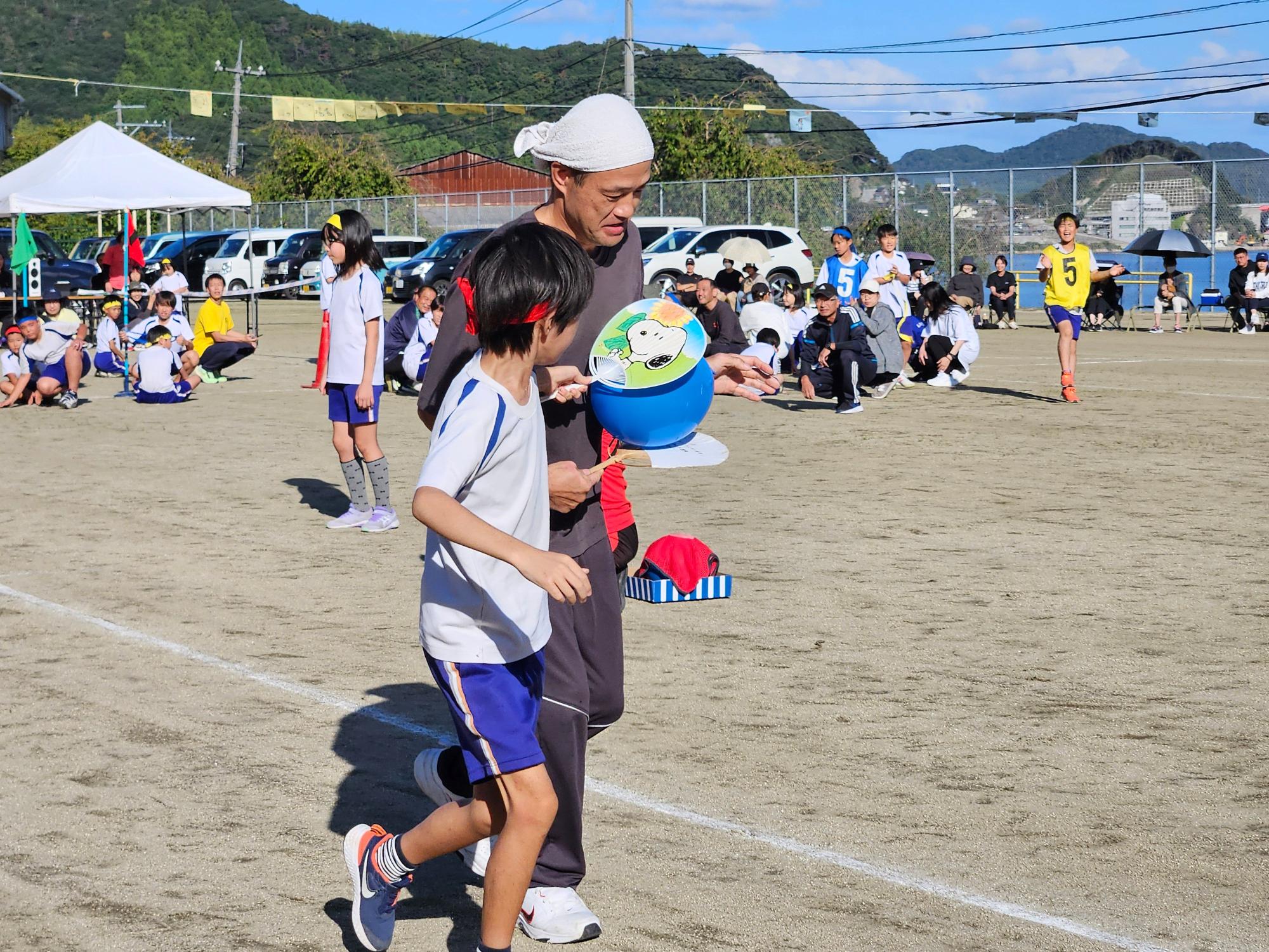 校庭で児童と大人が協力して競技をしている写真