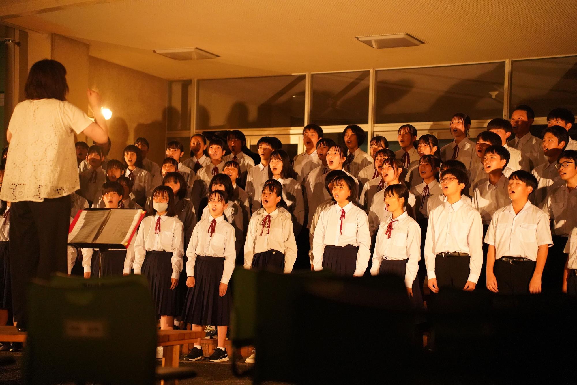 ホールの照明の下で生徒たちが合唱をしている写真