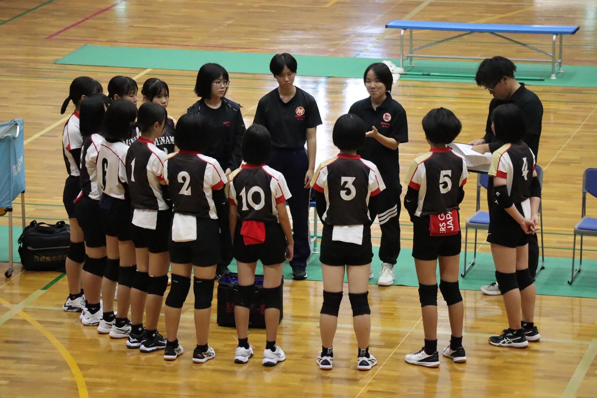 体育館で黒いユニフォームを着た女子生徒たちが円になって作戦会議をしている写真