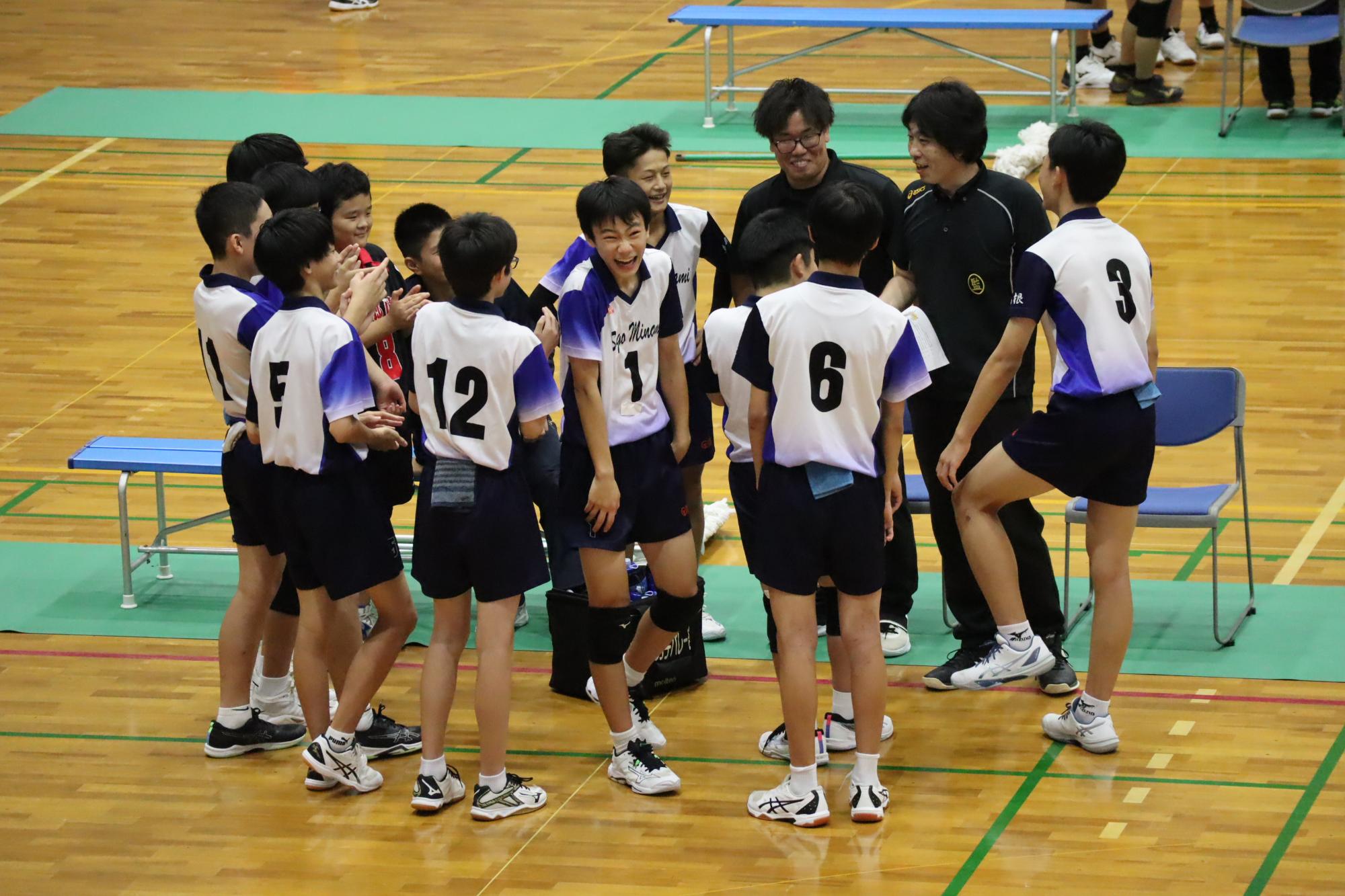 体育館で白いユニフォームを着た男子生徒たちが笑顔で作戦を確認している写真