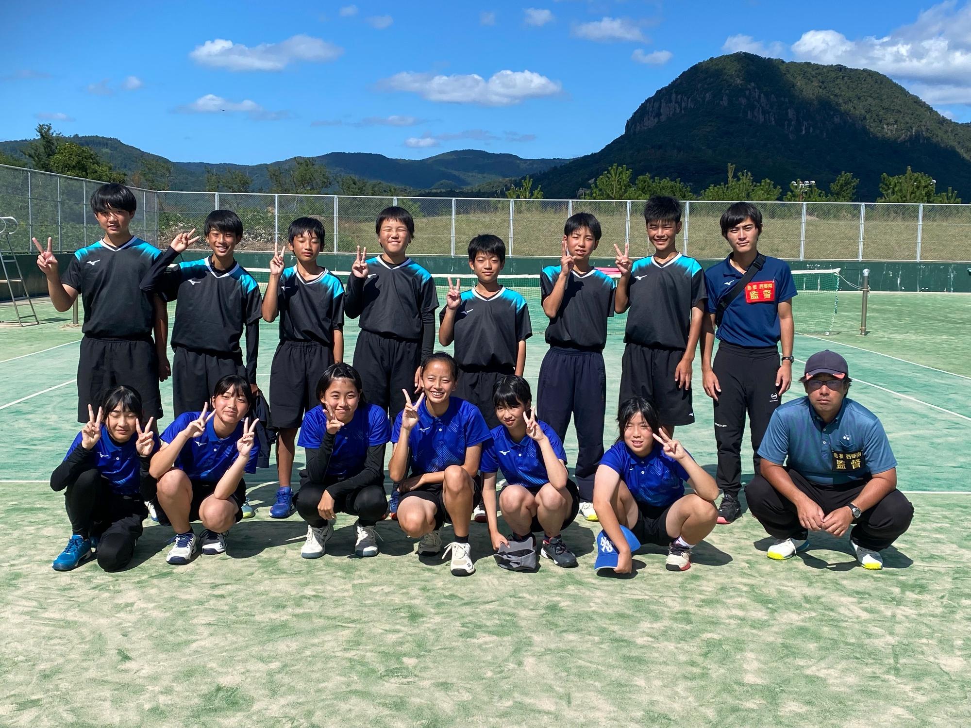 テニスコートで生徒たちとコーチが整列して記念撮影をしている写真