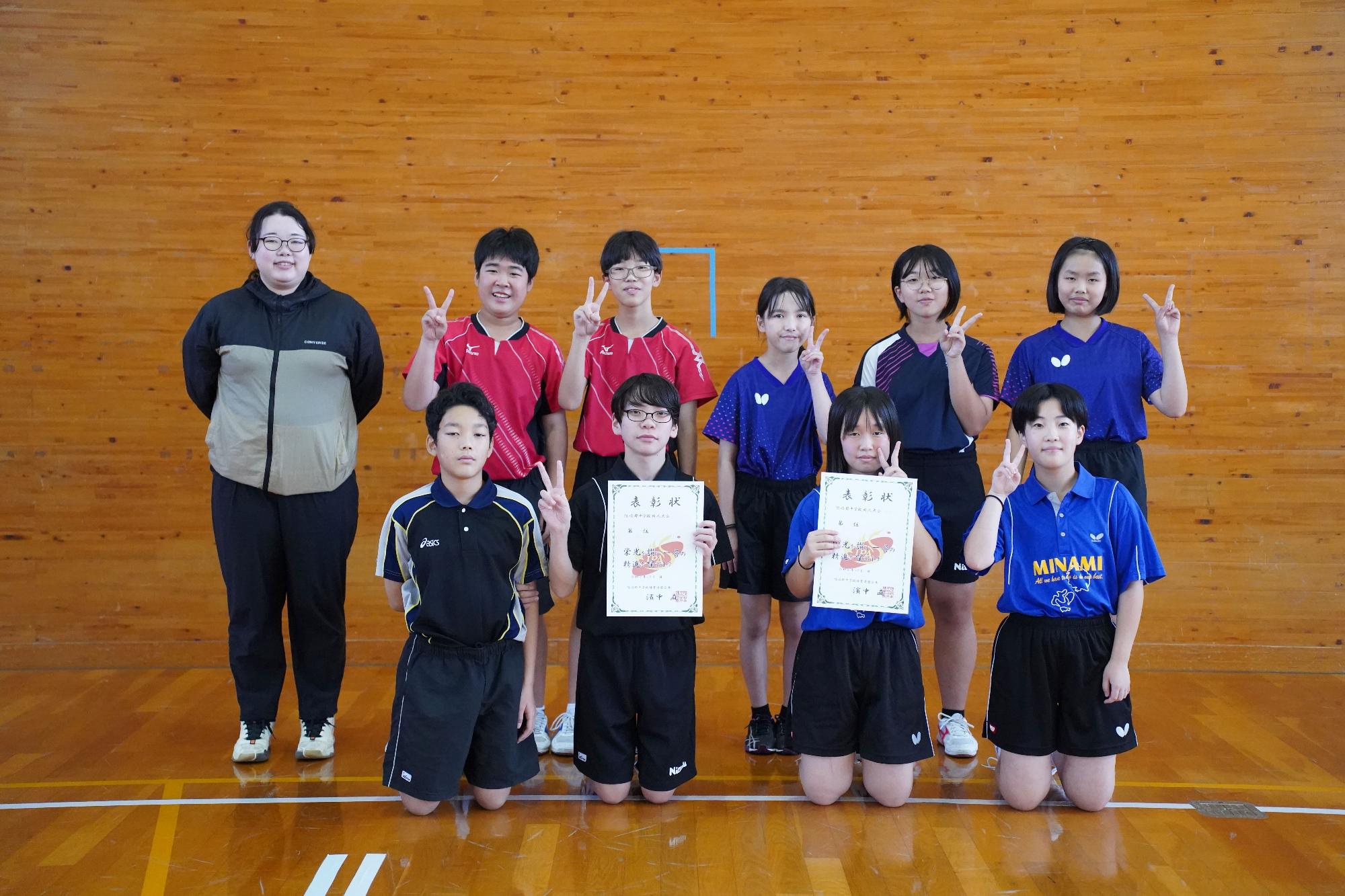 体育館で賞状を持った生徒たちが並んで記念撮影をしている写真