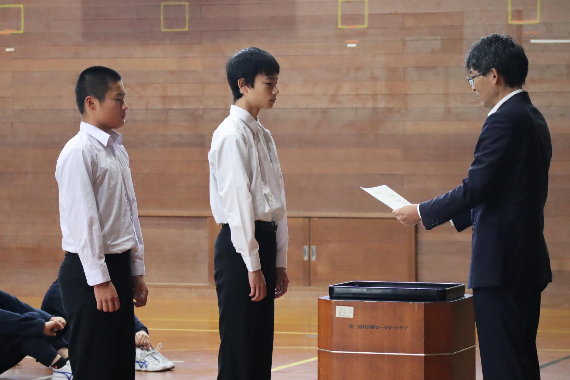 体育館で生徒が先生から表彰状を受け取っている写真