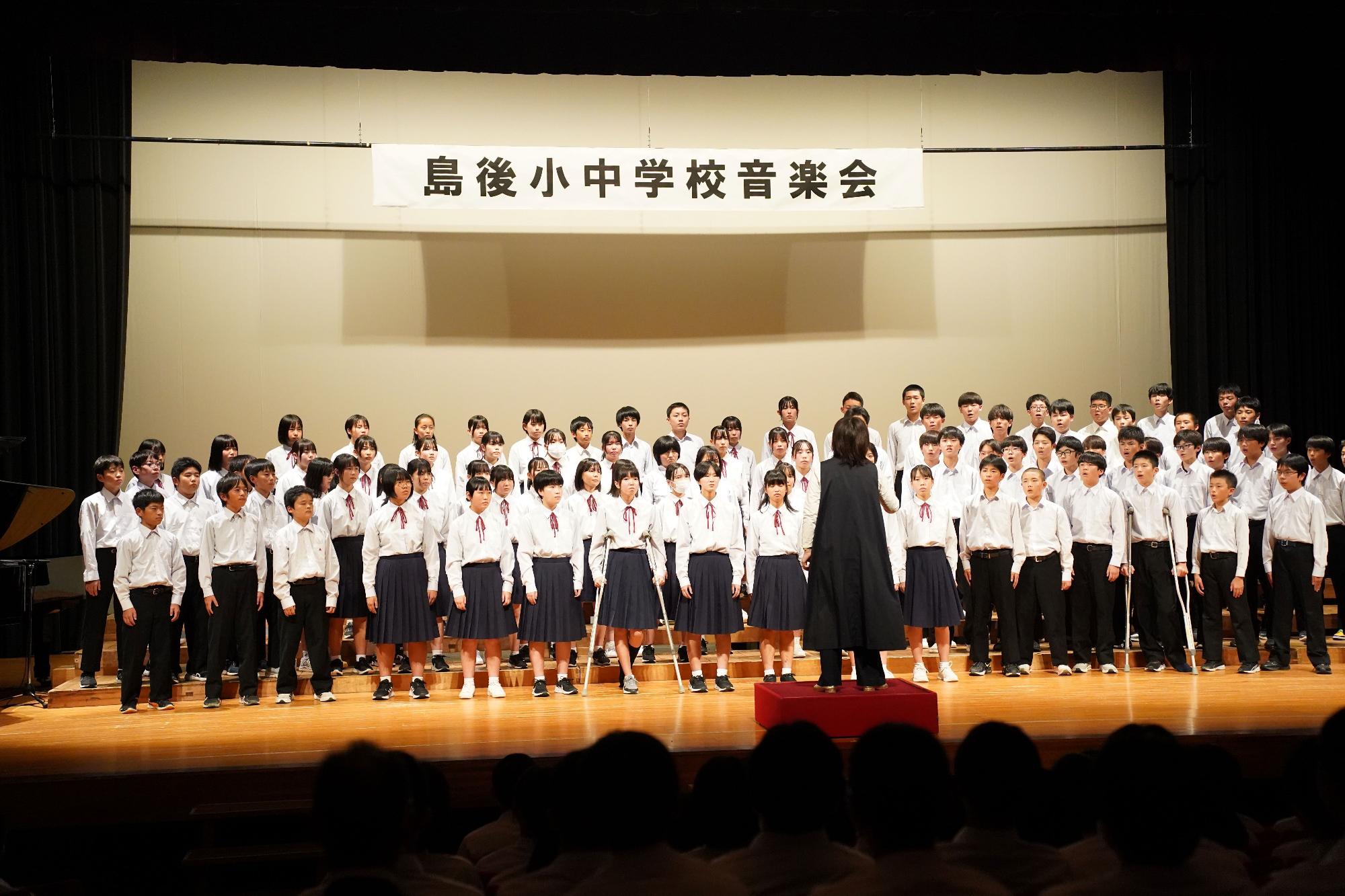 舞台上で生徒たちが指揮者に合わせて合唱している写真