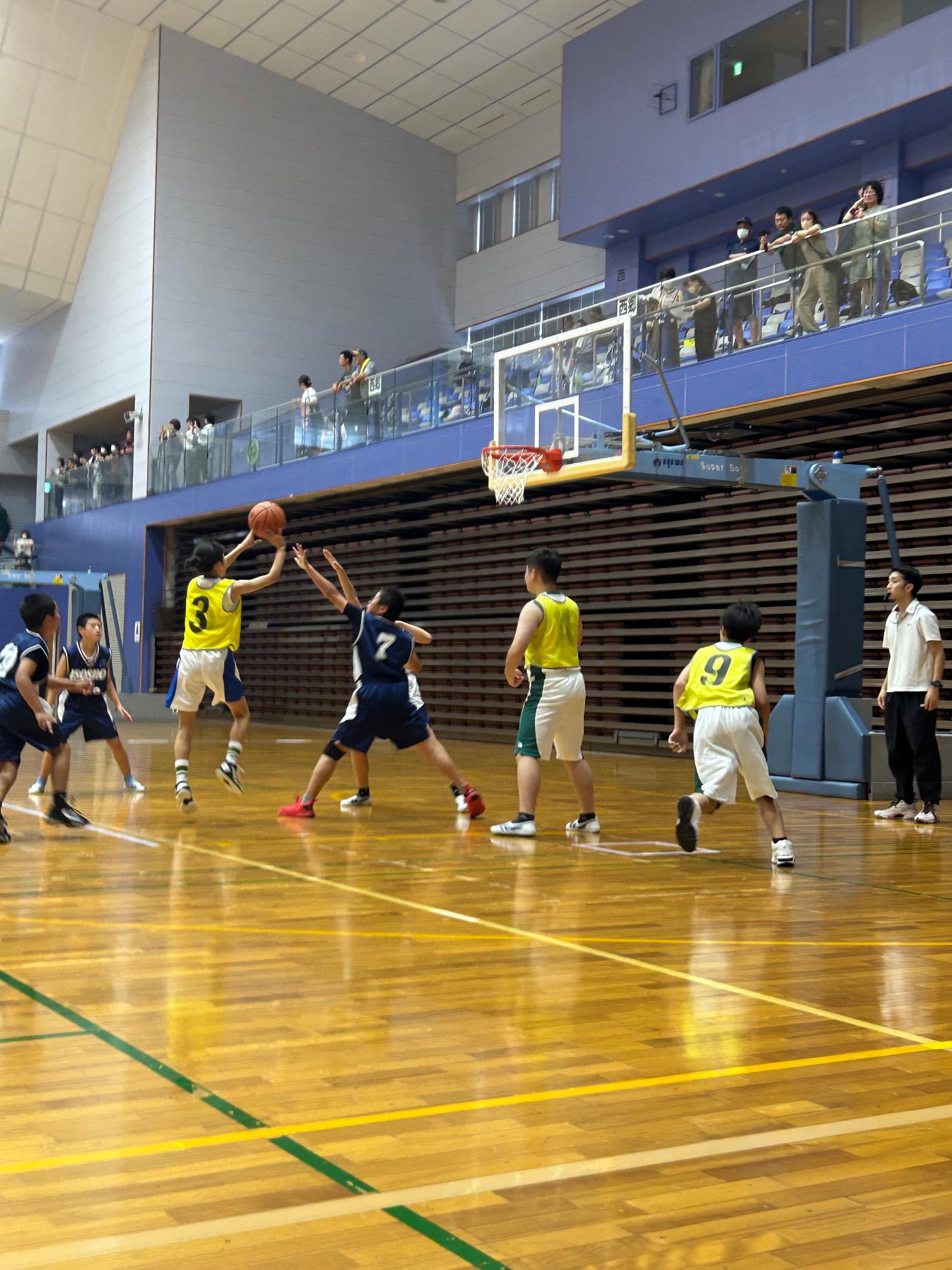 体育館のコートで児童たちがバスケットボールの試合をしている写真