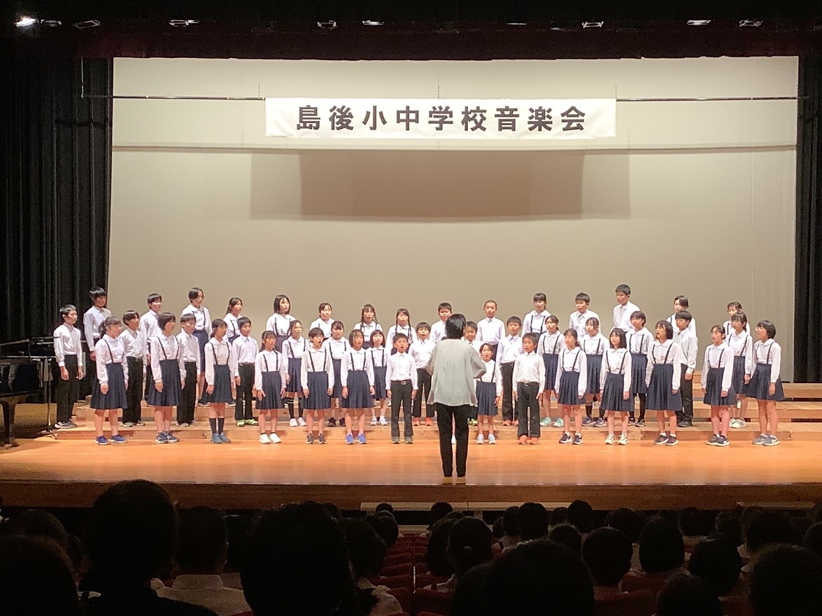 コンクール会場の舞台上で合唱をする児童と指揮者の写真
