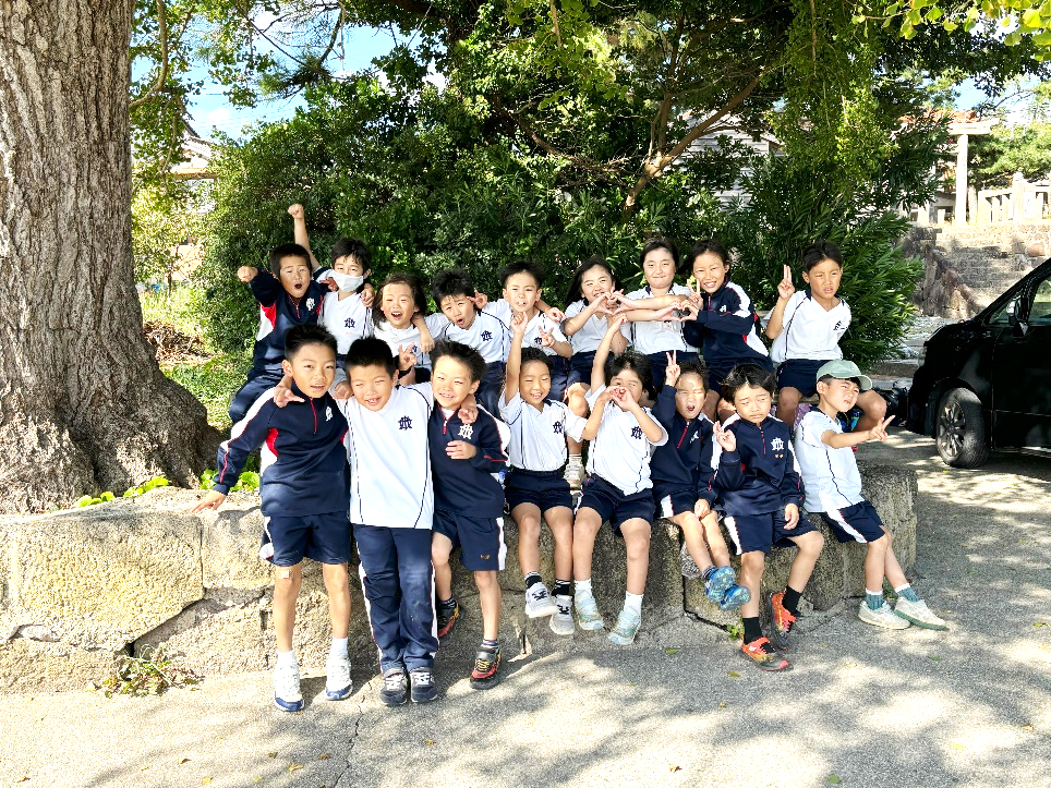 校庭の木の下で集合写真を撮る笑顔の児童たちの写真