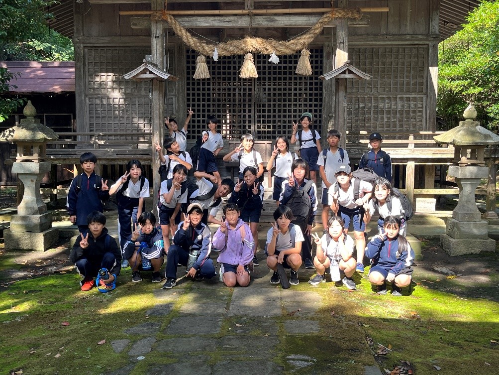 大きなしめ縄が飾られた神社の前で集合写真を撮る児童たちの写真