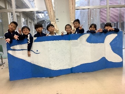 教室で大きなクジラの絵を広げる児童たちの写真