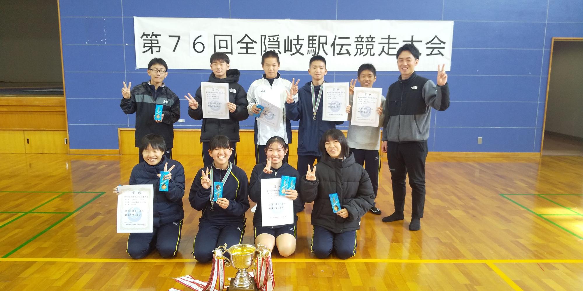 体育館で駅伝大会の表彰を受けた生徒たちが賞状を持って並んでいる写真