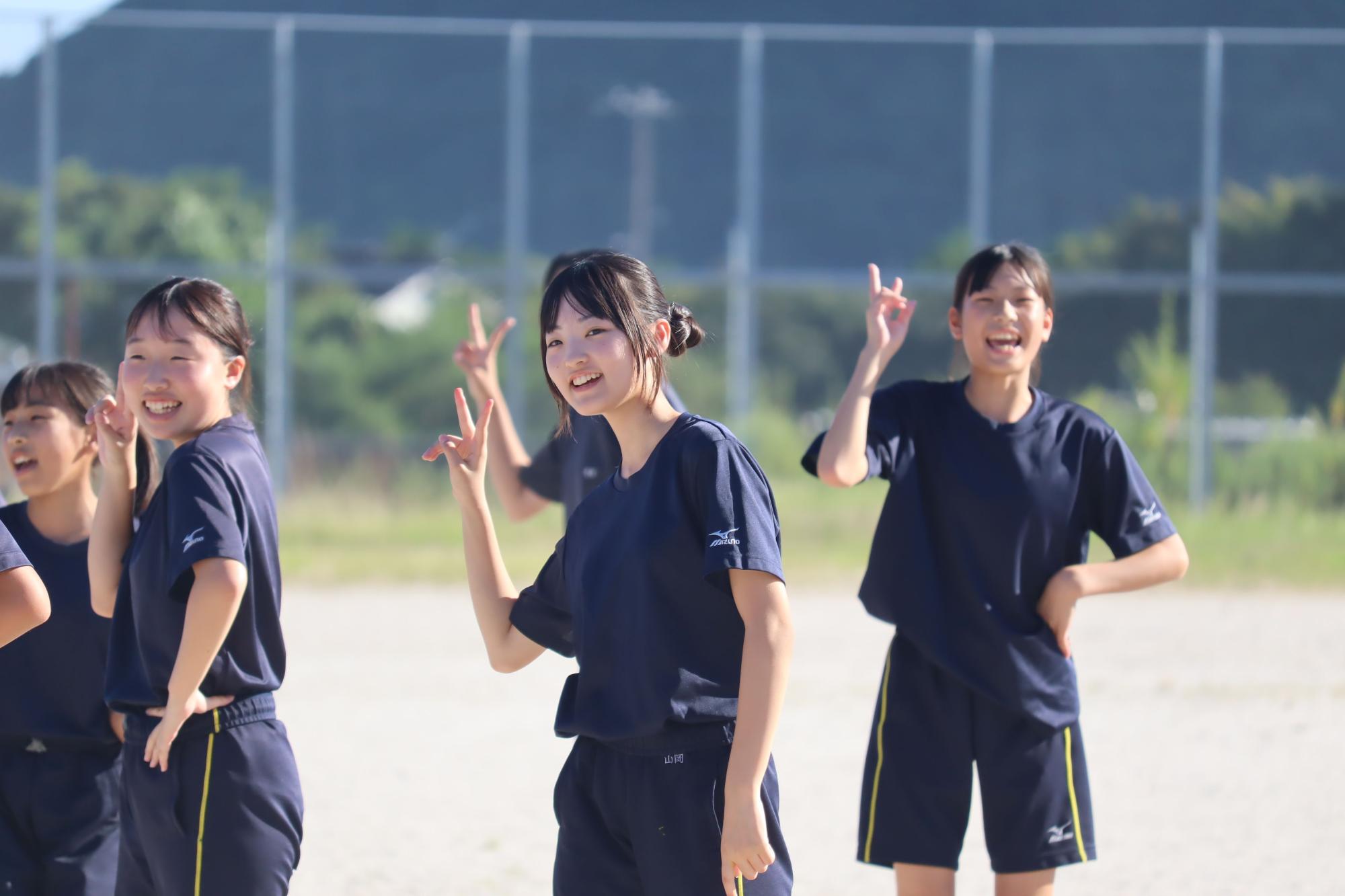 校庭で運動着を着た生徒たちが笑顔でポーズをとっている写真