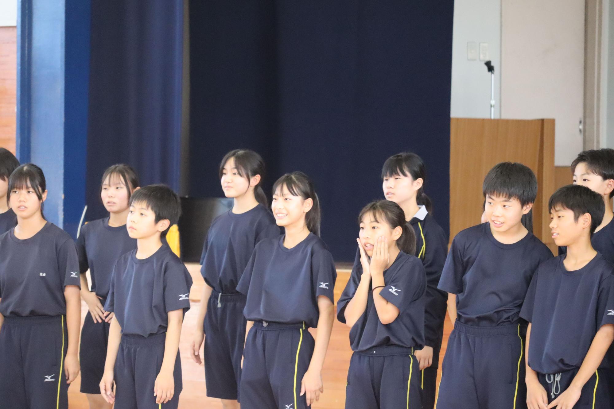 体育館で運動着を着た生徒たちが並んで発表をしている写真