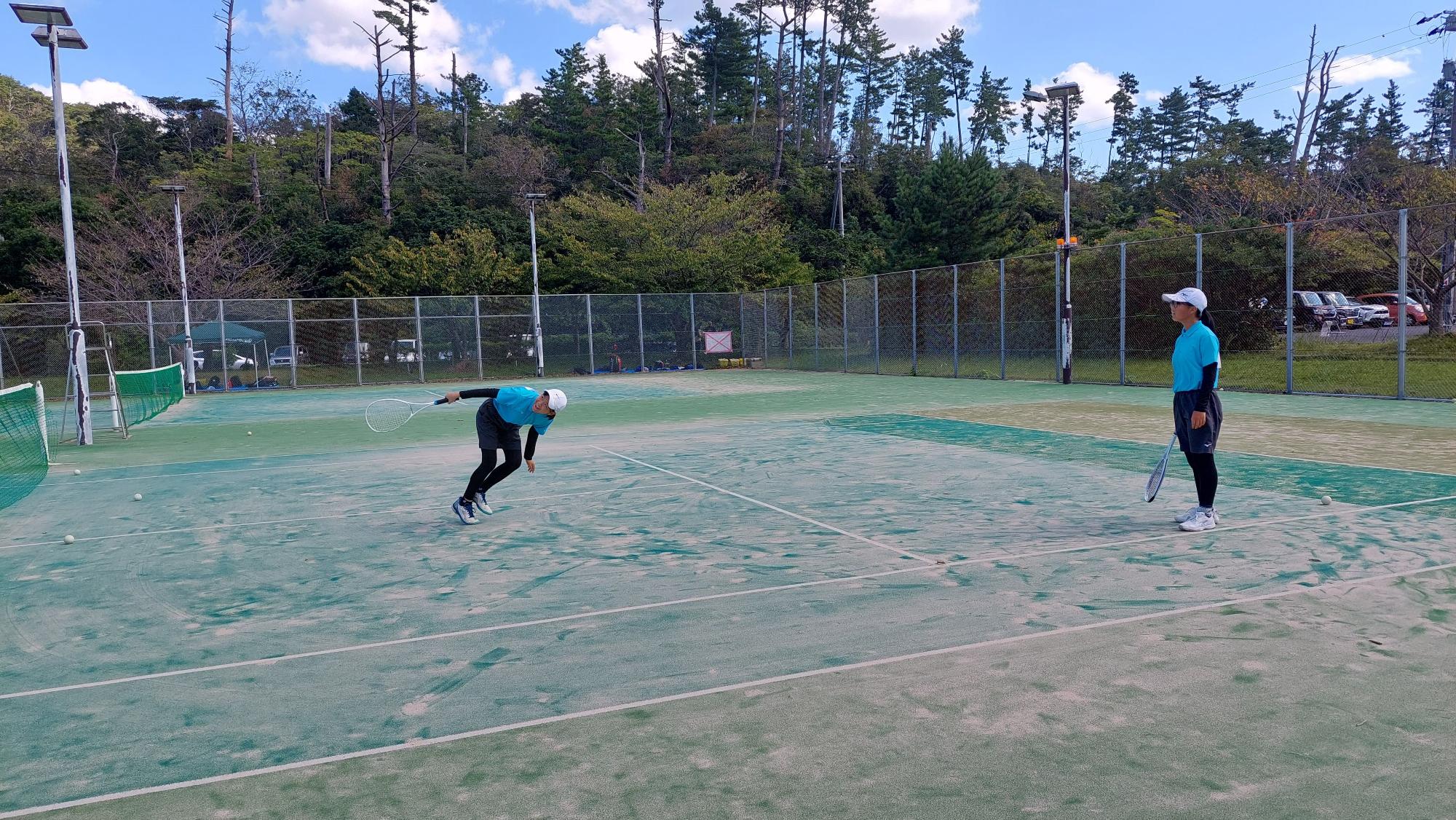 屋外テニスコートで生徒二名がテニスの打ち合いをしている写真